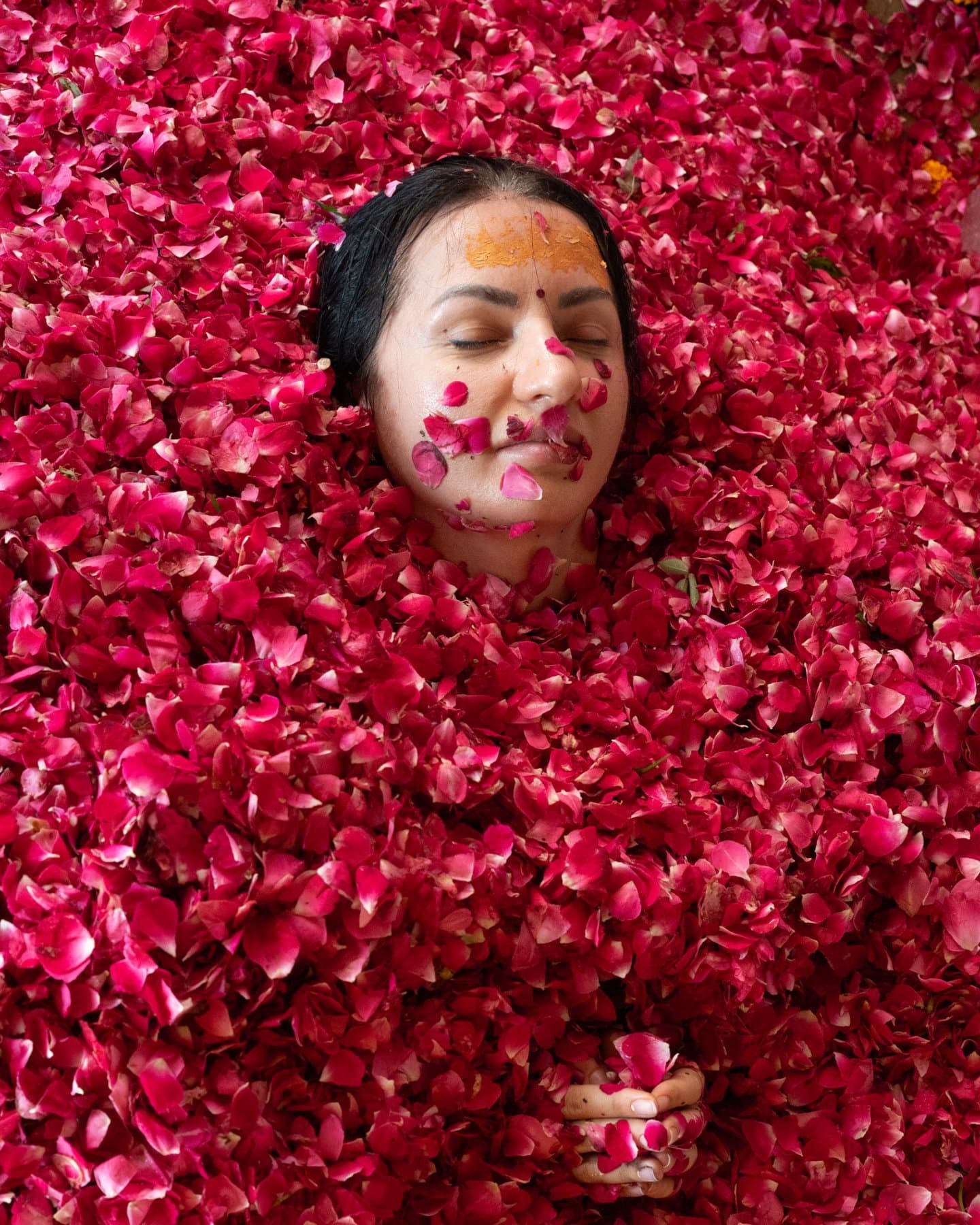 A participant with eyes closed, surrounded by rose petals during the Rose Rite