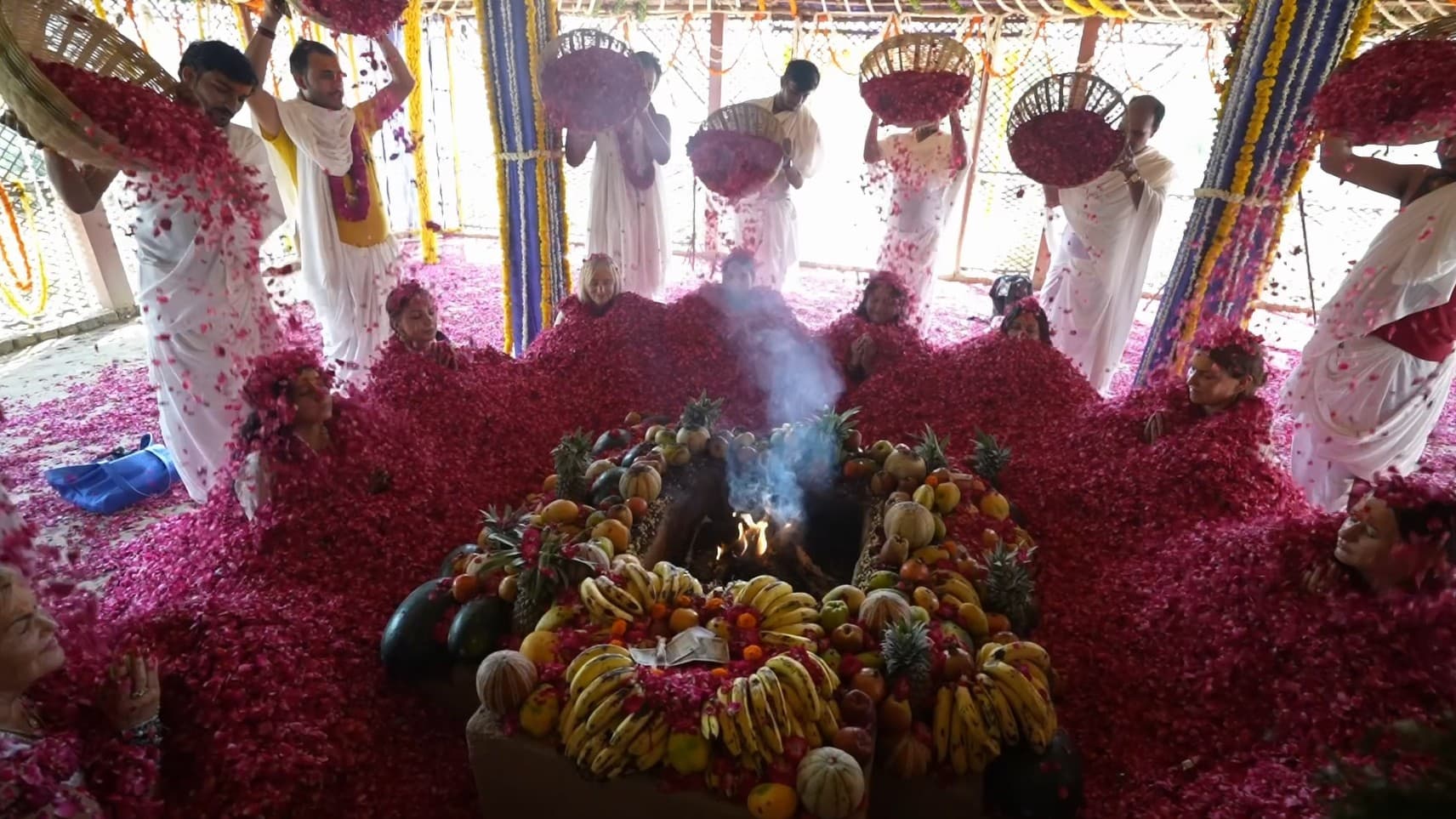 The Rose Ceremony — participants immersed in rose petals around the sacred fire and fruit offering as petals are poured from baskets, Vrindavan